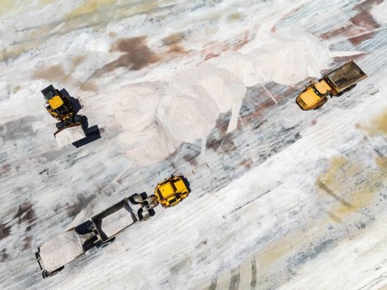 Excavator and lorries and at a harvesting pan of the Walvis Bay Salt works. Aerial view. Drone shot