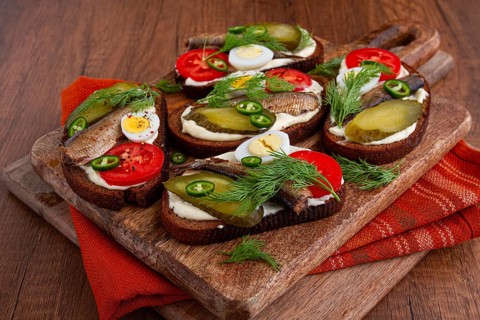 Sandwiches on rye bread with sprats, quail eggs, fresh tomatoes and pickled cucumber, on a wooden