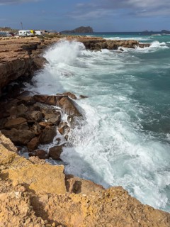 Coastal landscape with roaring waves crashing against rocky shores under a cloudy sky, Cala Conta