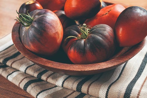 Freshly picked tomatoes, of the Black Beauty variety, in a wooden bowl, close-up, on the kitchen
