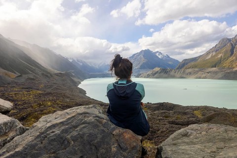 A woman sits on a rocky outcrop, taking in the breathtaking autumn scenery of Mount Cook, New