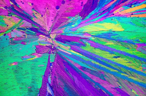 Close-up view of Adipic acid crystals under a microscope, showcasing a vibrant spectrum of purple,
