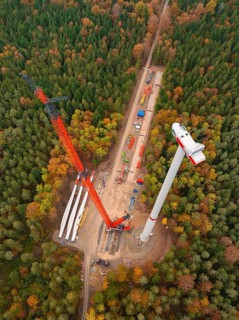 Construction of a wind turbine, crane lifts components in a colourful forest from a bird's eye