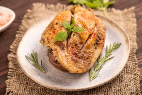 Fried Turkey Thigh with spices and rosemary on plate on brown wooden background and linen textile.