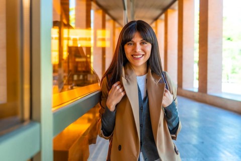 Young woman student standing confidently in a bright modern university corridor, smiling and ready