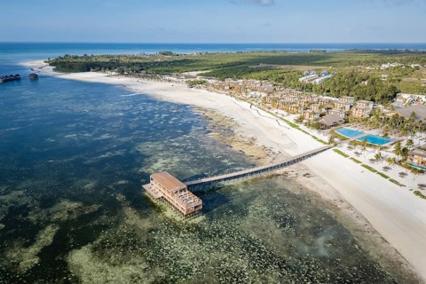 High angle aerial view of a luxury tropical resort on a white sand beach with a long wooden pier
