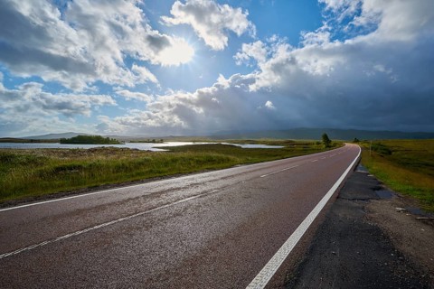 Sunny road along a vast landscape with expanses of water and threatening clouds in the sky, Rannoch