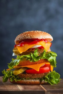 A tall, attractively decorated burger with fresh ingredients on a wooden board