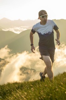 A man is trail running uphill in the early morning light, surrounded by stunning misty mountain