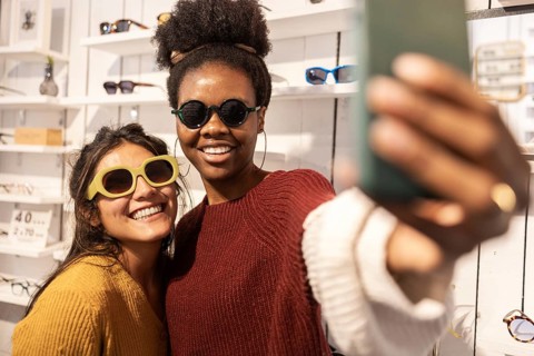 Two friends capture a joyful selfie inside a trendy sunglasses store, showcasing a variety of