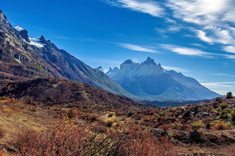 Majestic mountains rise under a sky with decorative cloud shapes over a vast landscape, The