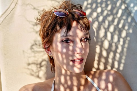 A young woman lounges on a sunbed at the beach, enjoying the summer warmth. Sunlight filters