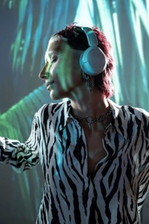 Young trendy woman enjoying music with headphones against vibrant background. Wearing zebra-striped