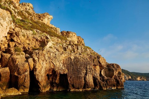 High rocky cliffs by the sea with sporadic growing vegetation, morning light, islet of Tsichli
