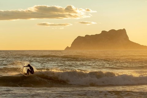A surfer catches a wave against the backdrop of a stunning sunset over the Mediterranean Sea on