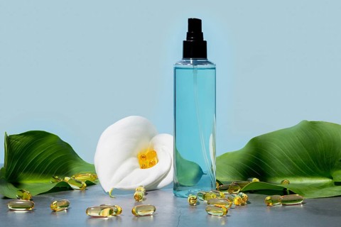 Elegant cosmetic spray clear blue bottle, paired with a fresh white calla lily and scattered omega