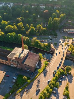 Aerial view of an industrial building with chimney, next to a road and cars, near a river and