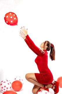 Pretty young woman in red dress playing with balloons. Studio portrait on white background.
