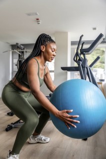 Concentrated businesswoman exercising with fitness ball in hotel gym during business trip,