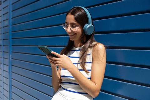 A woman in the city enjoys a sunny day, wearing headphones and using her smartphone, embodying the