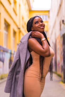 Trendy urban style with a black African girl in a cream colored dress on a city street. Posed with