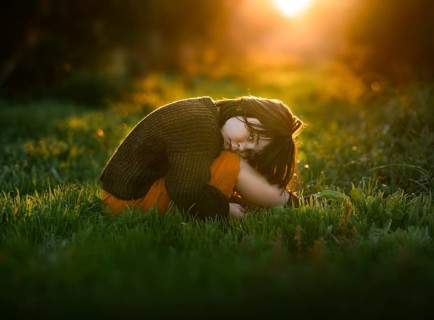 A young child, nestled on green grass with orange trees, basks in the serene glow of a sunset. The