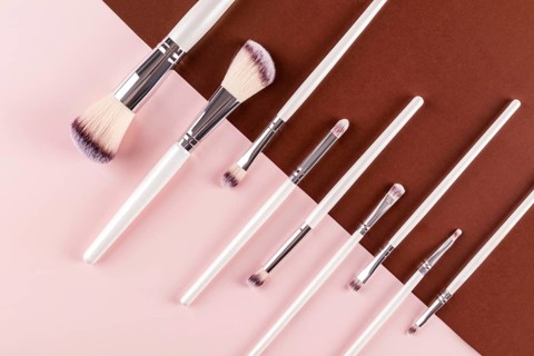 Elegant arrangement of various makeup brushes on a two toned pink and brown background. Perfect for