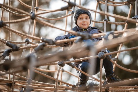 Cute boy in winter clothes on a rope construction at the playground