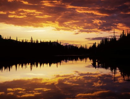 Clouds gather vivid colors at sunrise over Reflection Lake in Mount Rainier National Park,