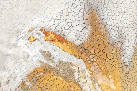 An abstract aerial view of cracked earth features a mesmerizing pattern in warm hues of orange,