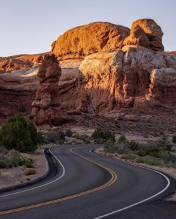A winding road leads through the iconic red rock formations of Arches national park, illuminated by