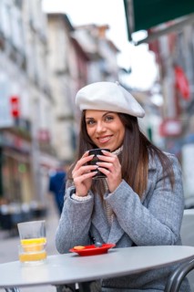 Vertical portrait of a woman with beret smiling at camera while drinking coffee outdoors