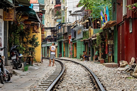 Railway line through a lively street with colourfully painted houses and a pedestrian, The Train