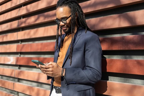 A cuban business man in a blue blazer uses a smartphone while leaning against a modern, striped