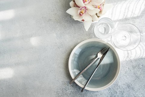 Overhead view of a minimalist dining setting. A cracked gray plate with fork and knife,