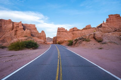 A scenic road curves between dramatic red rock formations under a clear sky in the arid desert of