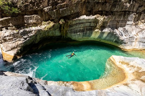 A canyoneer floats peacefully in a vibrant turquoise pool surrounded by curved canyon walls in