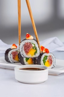 A close up view of vibrant sushi rolls filled with mango and tuna, topped with sauce. They are