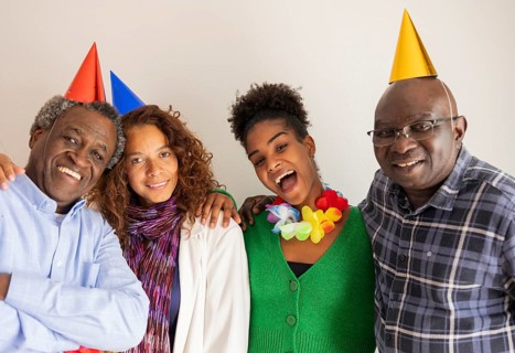 Happy friends wearing colorful party hats and leis, celebrating a birthday with wide smiles. A