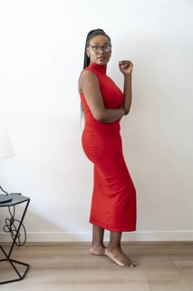 Confident businesswoman in red dress posing in modern hotel room during business trip, enjoying