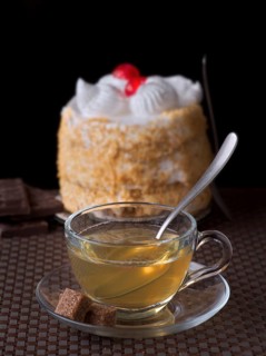 A warm cup of tea sits elegantly with a spoon on a glass saucer alongside cubes sugar. In the