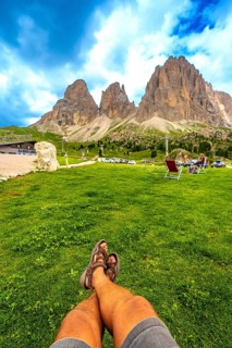 Point of view of tourist relaxing on the grass enjoying the sella pass in the dolomites in summer