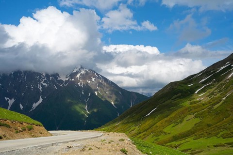 Road leads through mountains with clouds, blue sky and snow-capped peaks, Zagari Pass, Svaneti,