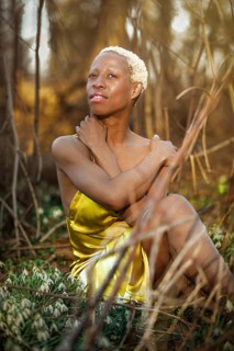 A woman in a vibrant golden dress sits thoughtfully in Tacony Creek Park. Her contemplative