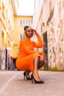Fashionable urban style with a black African girl in an orange dress and black heels on a city
