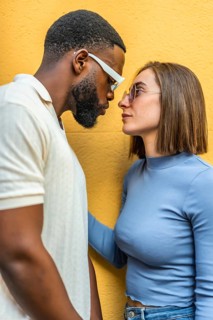 Vertical close-up side view of a cool modern couple looking at each other wearing sunglasses
