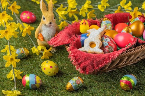 A basket full of colorful Easter eggs and a rabbit figurine with yellow flowers and chocolate eggs