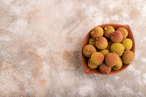 Ripe Lychee on clay bowl on brown concrete background, top view, flat lay, copy space, minimalism