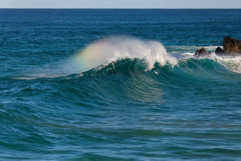 Waves crash against rocks at the mainland's easternmost point, creating rainbows in the ocean spray