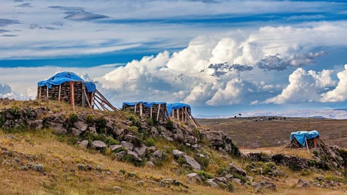 Structures covered with tarps, on a grassy hill under a cloudy sky, The Chullpas of Sillustani near